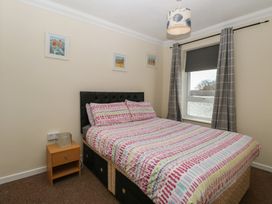 A bedroom with a bed with patterned bedding beside a wooden nightstand with a lamp and a window with curtains and a roller blind at No 108 Waterside in Corton