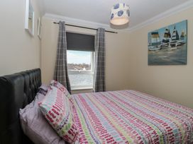 A bedroom with a bed covered in colorful patterned bedding a window with gray curtains and a painting of sailboats on the wall at No 108 Waterside in Corton
