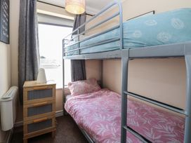 A small bedroom with a metal bunk bed next to a wooden chest of drawers and window at No 108 Waterside in Corton