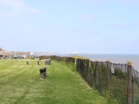A grassy area with benches and a chain link fence overlooking the sea at No 108 Waterside in Corton