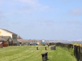 A grassy area with wooden benches near houses and a fenced edge overlooking water at No 108 Waterside in Corton
