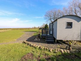 A small wooden cabin with steps and a bench on a grassy area with a clear sky at Little Acre in Oxenhope