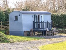 A small gray cabin with a porch and two wooden chairs outside on gravel at Little Acre in Oxenhope