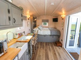 A compact room with a kitchenette on the left and a bed at the back with a small TV on the wall at Little Acre in Oxenhope