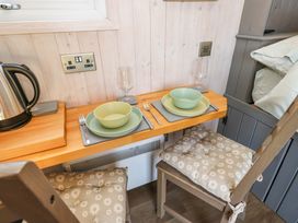A small dining area with two place settings including plates bowls glasses and cutlery with cushioned chairs and a kettle on a wooden counter at Little Acre in Oxenhope