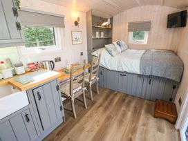 A small room with a bed shelf kitchen counter two chairs and a wall-mounted tv at Little Acre in Oxenhope
