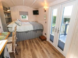 A small room with a bed, small dining table with chairs, wall-mounted television and glass doors leading outside at Little Acre in Oxenhope