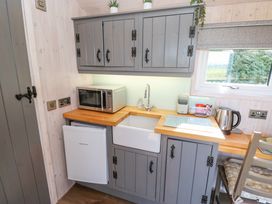 A compact kitchen area with gray cabinets a wooden countertop a microwave a small refrigerator a sink a kettle and a window at Little Acre in Oxenhope