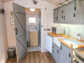 A kitchen with grey cabinets wooden countertops a white sink a microwave and a small fridge next to a doorway leading to a bathroom at Little Acre in Oxenhope