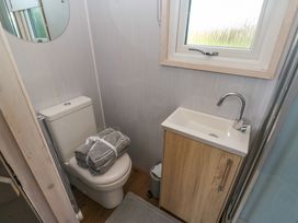 A small bathroom with a toilet holding folded towels a sink with a cabinet a window and a round mirror at Little Acre in Oxenhope