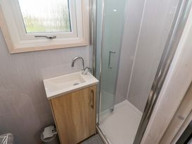 A small bathroom with a wooden vanity cabinet and a white sink next to a glass shower enclosure at Little Acre in Oxenhope