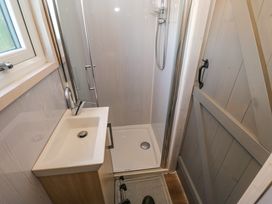 A small bathroom with a sink and faucet next to a shower and a wooden door at Little Acre in Oxenhope