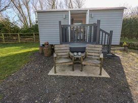 An outdoor seating area with two wooden chairs and a table with mugs in front of a small gray cabin with open doors and stairs at Little Acre in Oxenhope