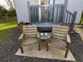 Two wooden chairs with a small table holding two mugs on a patio outside a grey building at Little Acre in Oxenhope