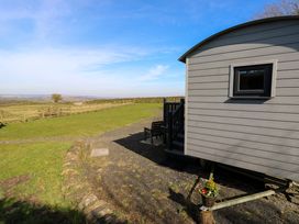 A small grey wooden cabin with a window and outdoor stairs with chairs on a grassy field at Little Acre in Oxenhope