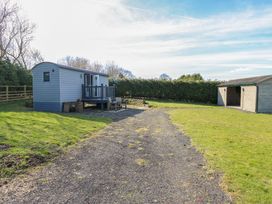 A small gray cabin with a porch and outdoor chairs on a gravel path next to a wooden shed in a grassy yard at Little Acre in Oxenhope