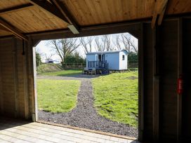 A small white cabin with stairs and outdoor seating on grass viewed from inside a wooden structure at Little Acre in Oxenhope