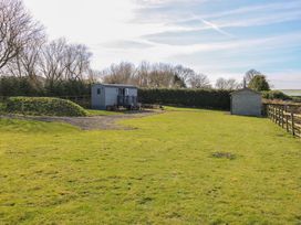 A grassy field with a small grey cabin and a shed surrounded by trees and a wooden fence at Little Acre in Oxenhope