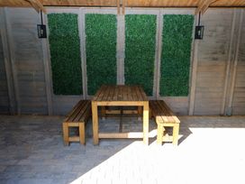 An outdoor seating area with a wooden table and two benches against a wall with green vertical plant panels