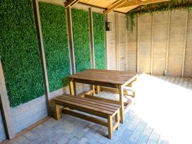 A wooden table with benches on a paved floor with artificial green panels on walls at Little Acre in Oxenhope