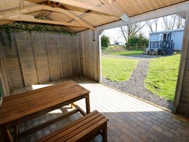 A wooden gazebo with picnic benches overlooking a grassy yard with a path leading to a small cabin and outdoor seating at Little Acre Oxenhope