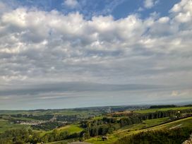 A landscape view of green rolling hills with a village and wind turbines under a cloudy sky at Little Acre in Oxenhope