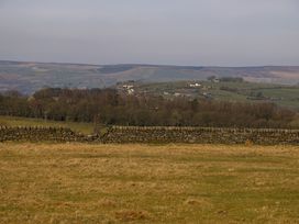 A stone wall with a grassy field and hills with houses and trees at Little Acre in Oxenhope