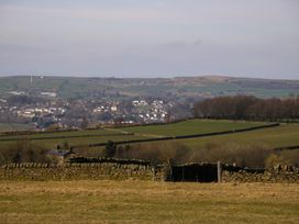 A rural landscape with stone walls and green fields with a village and hills in the background at Little Acre in Oxenhope