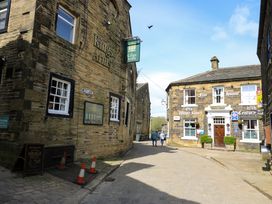A cobblestone street with two people walking past buildings including The Kings Arms and Old White Lion in Oxenhope