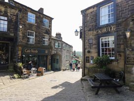 A cobblestone street with Cafe Verde and Black Bull buildings and outdoor seating at Little Acre in Oxenhope