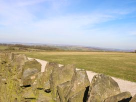 A stone wall with a grassy field and a dirt path under a blue sky at Little Acre in Oxenhope