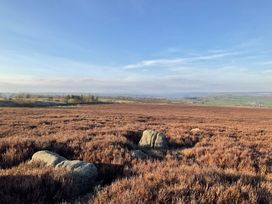A field with brown vegetation and rocks under a blue sky with distant hills at Little Acre in Oxenhope