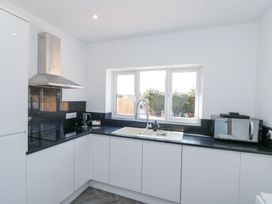 A kitchen with white cabinets a black countertop a sink under a window a microwave a kettle and a stainless steel extractor hood at The Hideaway in Bempton near Flamborough