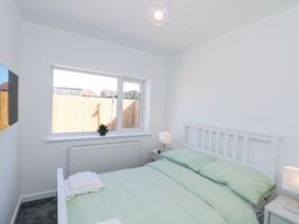 A bedroom with a double bed with green bedding bedside tables with lamps a window and a wall-mounted television at The Hideaway in Bempton near Flamborough