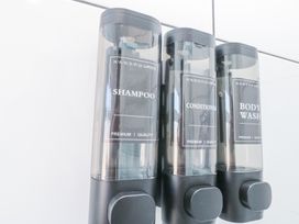 Three wall-mounted dispensers labeled shampoo conditioner and body wash in a bathroom