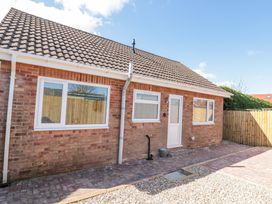 The exterior of a single-story brick house with three windows a white door a tiled roof and a paved and gravel area at The Hideaway in Bempton near Flamborough