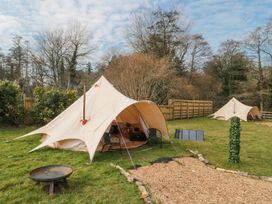 Two beige bell tents set up on grass with chairs and a fire pit outside at Bell tent 2 in Camerton near Timsbury