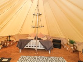 A bed with pillows and blankets inside a bell tent with wooden crates and a hanging candle holder at Bell tent 2 in Camerton near Timsbury