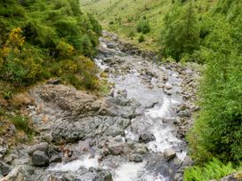 A river flowing through rocks and greenery at Swirral Edge Cottage in Glenridding