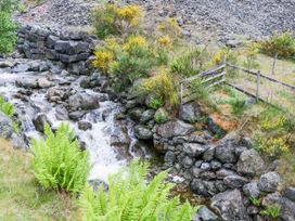 A stream flowing over rocks with ferns and a wooden fence at Swirral Edge Cottage in Glenridding