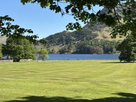 A grassy area with trees and a lake at Swirral Edge Cottage in Glenridding