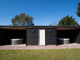 Two outdoor hot tubs on either side of a black wooden structure with a white door in the middle at Driftwood in Kessingland