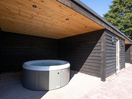 A hot tub under a wooden roof outside a black wooden building at Driftwood in Kessingland