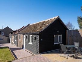 A black wooden building with a tiled roof next to an outdoor dining table and chairs on a paved patio at Driftwood in Kessingland