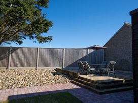 A backyard with a pebble area wooden fence and a patio set with chairs and an umbrella at Driftwood in Kessingland