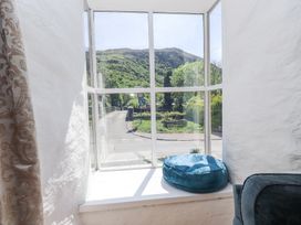 A window with a blue cushion on the sill overlooking a road and green hills at Llys Emrys in Beddgelert