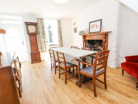A dining room with a wooden table and six chairs a grandfather clock curtains a fireplace and a red armchair at Llys Emrys in Beddgelert