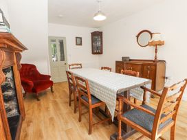 A dining room with a table covered in a tablecloth surrounded by wooden chairs a red armchair a wooden cabinet with a lamp and a round mirror on the wall at Llys Emrys in Beddgelert