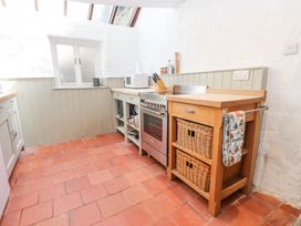 A kitchen with terracotta floor tiles a stove microwave knife block and wicker baskets at Llys Emrys in Beddgelert