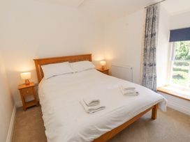 A bedroom with a wooden bed frame white bedding bedside tables with lamps and a window with patterned curtains at Llys Emrys in Beddgelert